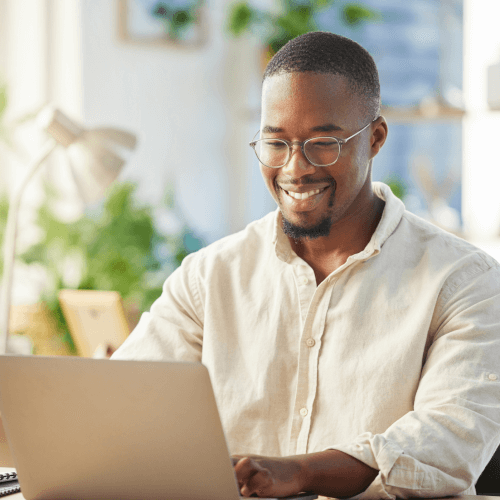 A smiling person engaged in work on payroll software on a laptop in a bright, plant-filled room.